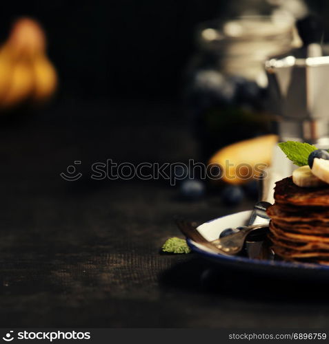 Pancake tower with fresh bananas, blueberries and honey on a rustic table