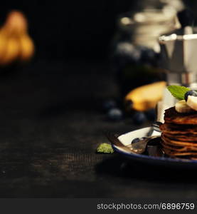 Pancake tower with fresh bananas, blueberries and honey on a rustic table