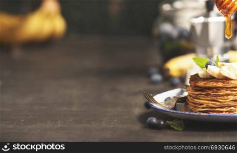 Pancake tower with fresh bananas, blueberries and honey on a rustic table