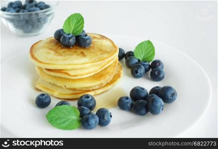 Pancakes breakfast background with a stack of pancakes with blueberries, mint leaves and maple syrup.