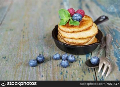 Pancakes in cast-iron frying pan with fresh berries on the background of the old wooden boards
