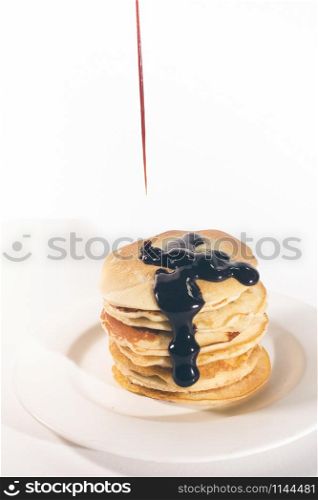 pancakes, stacked on a white plate, are topped with chocolate.