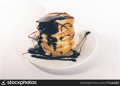 pancakes, stacked on a white plate, are topped with chocolate.