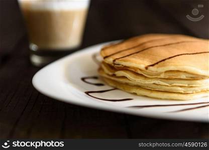 pancakes with chocolate topping and coffee cappuccino with corica on the table