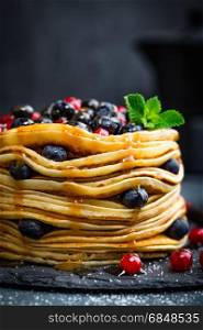 Pancakes with fresh berries and maple syrup on dark background, closeup