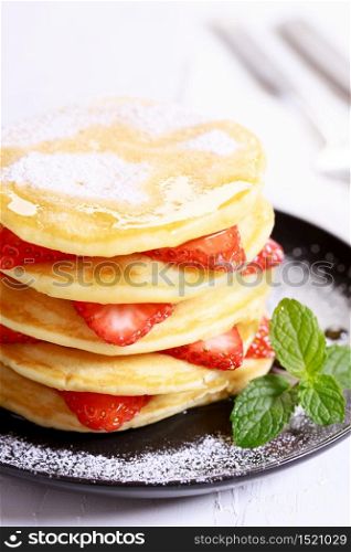 Pancakes with fresh strawberry slices and maple syrup on black plate
