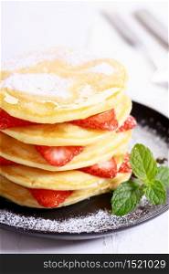 Pancakes with fresh strawberry slices and maple syrup on black plate