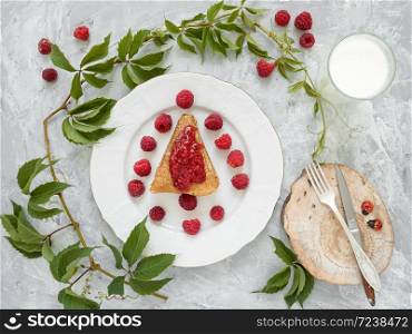 Pancakes with jam are located on a white plate, around the pancakes on a plate are fresh berries. Next to a glass of milk. Breakfast, festive food. Gray background. View from above.