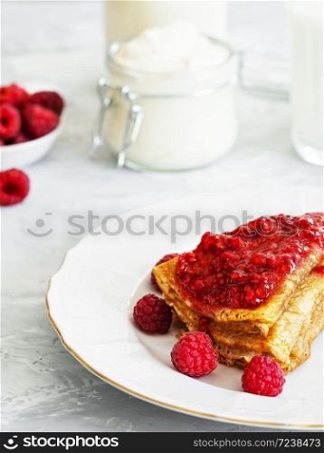 Pancakes with jam are located on a white plate, around the pancakes on a plate are fresh berries. Next to a glass of milk and sour cream. Breakfast, festive food, christmas. Gray background. Close-up.