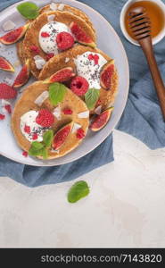 Pancakes with raspberries, figs, yogurt, coconut zest, honey and mint leaves on a plate