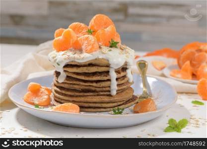 Pancakes with yogurt and tangerines on a light modern kitchen counter top with oat, thyme and mint leaves.