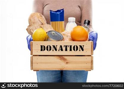 pandemic and charity concept - close up of woman in gloves with food donation in wooden box on white background. woman in gloves with food donation in wooden box
