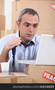 Panicking man using a laptop surrounded by boxes