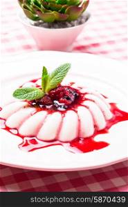 Panna cotta with berry sauce and mint leaf close up
