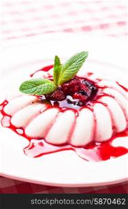 Panna cotta with berry sauce and mint leaf close up