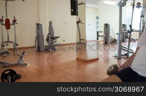 Panning shot of a mature man exercising with dumb-bells in the gym