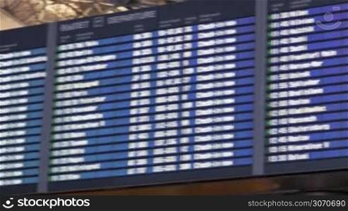 Panning shot of digital flight schedule at the aiport. It is shown on four big displays