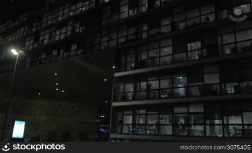 Panning shot of modern glassy office building or business centre at night