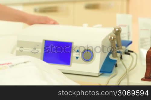 Panning shot of turning on the equipment and choosing settings while a woman waiting with cosmetic mask on her face