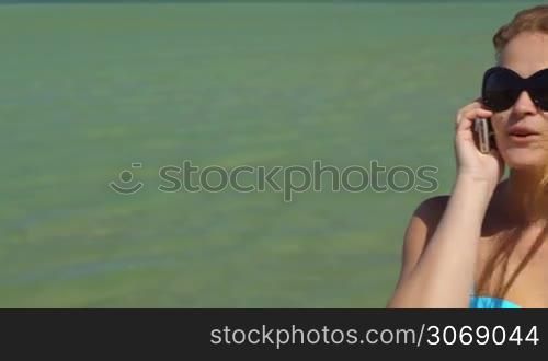 Panning shot of young woman talking on the phone by the sea on a windy day