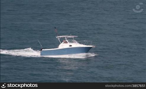 Panning with a recreational boat in the ocean, then it exits off frame
