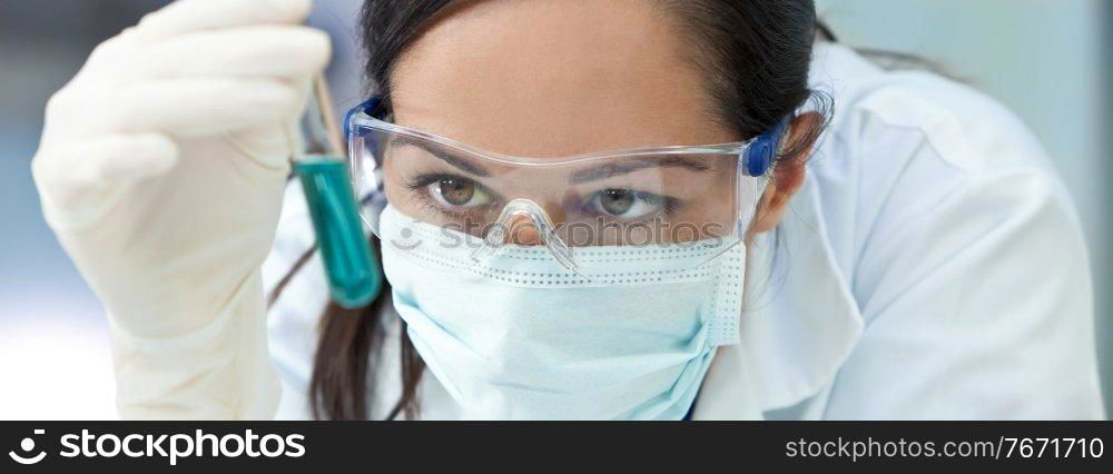 Panorama female medical or scientific researcher or doctor wearing a face mask looking at a test tube of liqud blue solution in a laboratory panoramic web banner header