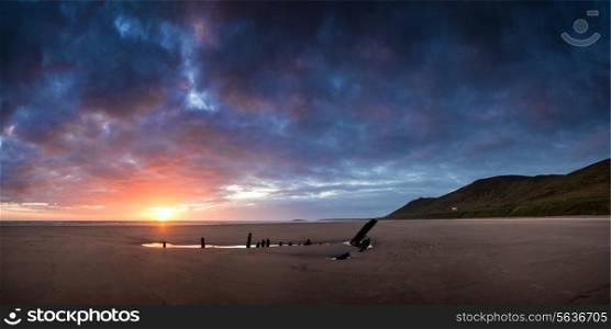 Panorama landscape image of shipwreck on beach at sunset in Summer