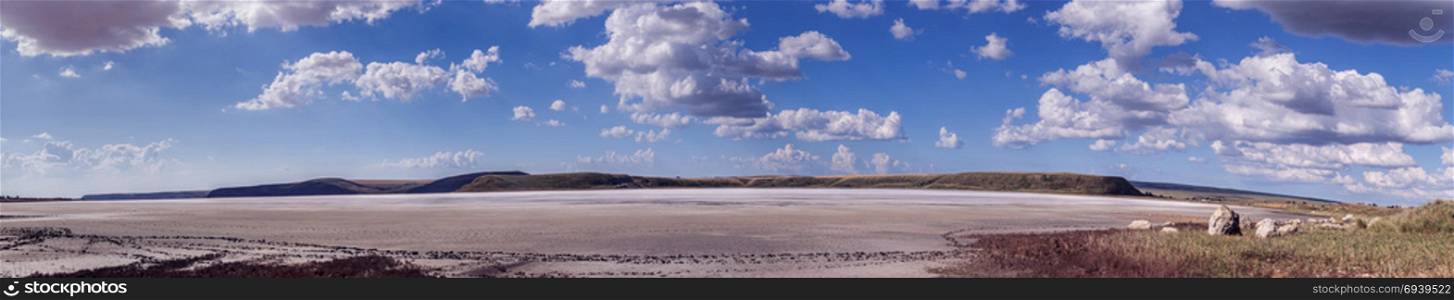 Panorama of a dried salt lake. Dry lake against the backdrop of mountains and cloudy sky. Panorama
