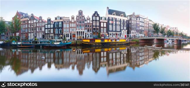 Panorama of Amsterdam canal Singel with typical dutch houses, bridge and houseboats during morning blue hour, Holland, Netherlands.