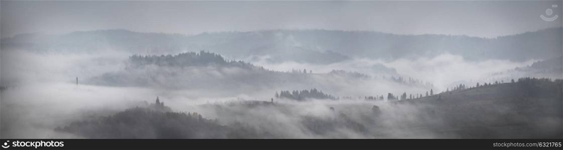 Panorama of autumn rain and fog on the mountain hills. Misty fall woodland. Forest on hills in clouds of fog