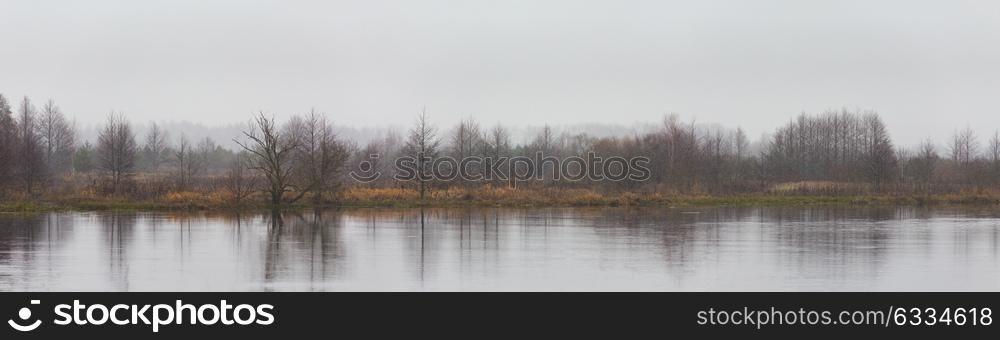 Panorama of autumn river landscape. Snowfall, cloudy weather. Overcast climate. Winter Is Coming.