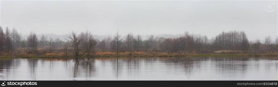 Panorama of autumn river landscape. Snowfall, cloudy weather. Overcast climate. Winter Is Coming.