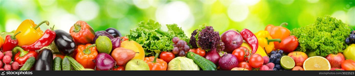 Panorama of fresh vegetables and fruits on natural blurred background of green leaves.