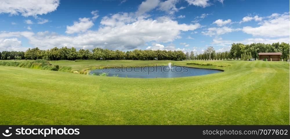 Panorama of golf course with pond in sunny summer day