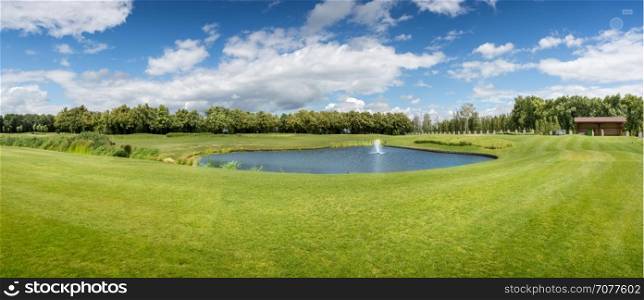Panorama of golf course with pond in sunny summer day