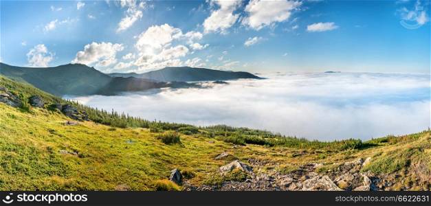 Panorama of green mountains in the clouds. Landscape view on green hills in fog at sunset