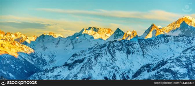Panorama of high mountains peaks at sunset. Landscape on snow hills
