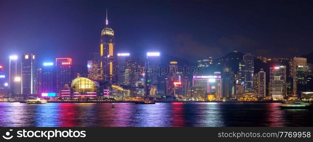 Panorama of Hong Kong skyline cityscape downtown skyscrapers over Victoria Harbour in the evening illuminated tourist boats and ferries . Hong Kong, China. Hong Kong skyline. Hong Kong, China