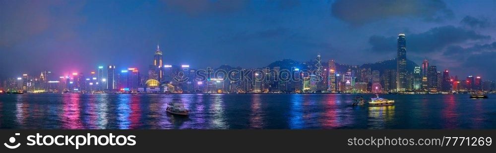 Panorama of Hong Kong skyline cityscape downtown skyscrapers over Victoria Harbour in the evening illuminated with tourist boat ferries . Hong Kong, China. Hong Kong skyline. Hong Kong, China
