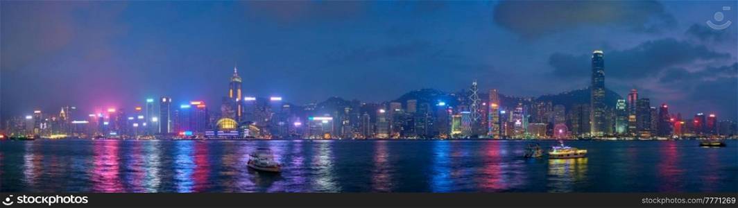 Panorama of Hong Kong skyline cityscape downtown skyscrapers over Victoria Harbour in the evening illuminated with tourist boat ferries . Hong Kong, China. Hong Kong skyline. Hong Kong, China