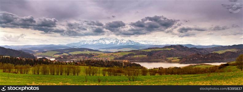Panorama of snowy Tatra mountains in spring, south Poland. Malopolska. Lake and village behind high mountain range. Cloudy spring day panorama landscape.
