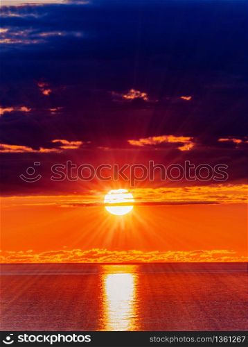 Panorama of sun in dark clouds and sea water surface at sunset