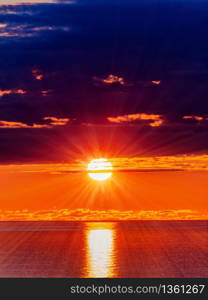 Panorama of sun in dark clouds and sea water surface at sunset