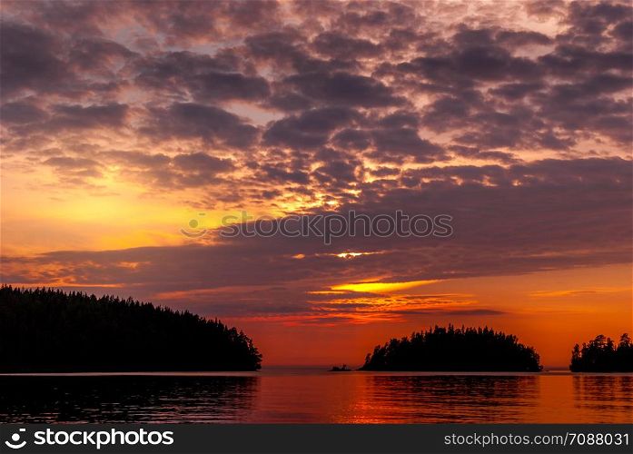 Panorama of the lake at sunset. The setting sun behind the clouds and the silhouettes of the islands. Panorama of the bay on Lake Ladoga at sunset.