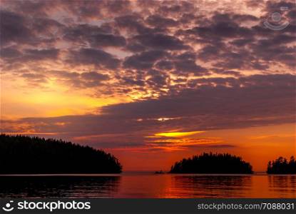 Panorama of the lake at sunset. The setting sun behind the clouds and the silhouettes of the islands. Panorama of the bay on Lake Ladoga at sunset.