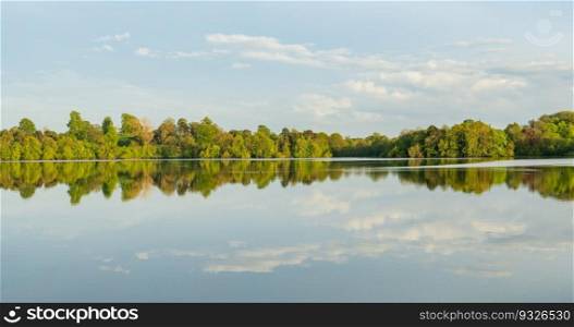 Panorama of the lake shore of the Mere with a perfect lake reflection in Ellesmere in Shropshire. View across the Mere to a clear reflection of distant trees in Ellesmere