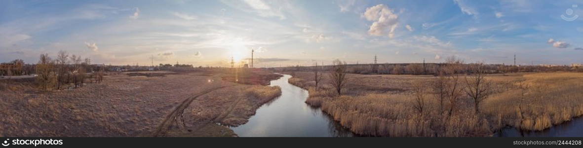 Panorama of the river with power towers in the background. Dry reeds along the shore. Sunset. Panorama of river with power towers in background