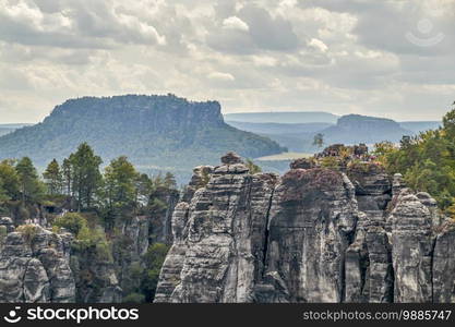 Panorama of the Saxon Switzerland trekking and climbing aera in the Elbe Sandstone Mountains with a dramatic cloudy sky and the rock formations called Ferdinandstein, an the elevations Lilienstein and Kingstone in the background. View from the sightseeing point called pavilion. Panorama Saxon Switzerland of the rock formations Ferdinandstein, Lilienstein and Konigstein