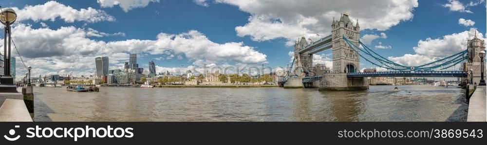 Panorama of Tower Bridge, the Tower of London and the city with the river Thames in foreground with blue skies and fluffy clouds
