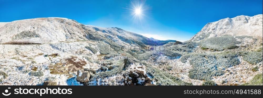 Panorama of white mountains with snow and bright shining sun and sunrays
